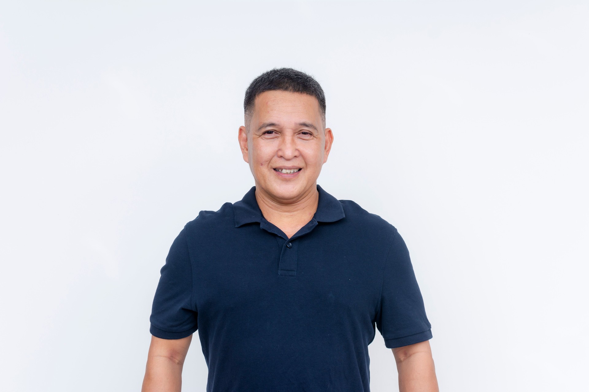 Portrait of a cheerful middle-aged Asian man dressed casually in a dark polo shirt, isolated on a white background.